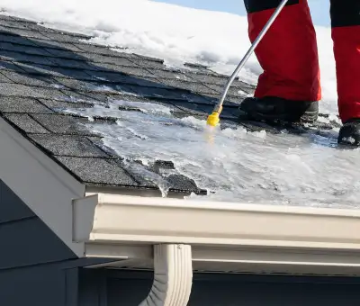 Ice dam removal technician using a steam wand to melt thick ice buildup on a residential roof in Erie, PA