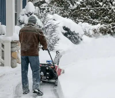 Residential snow removal technician using a snow blower to clear a home driveway and walkway in Erie, PA